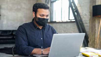 man in an office on a laptop while holding mobile phone