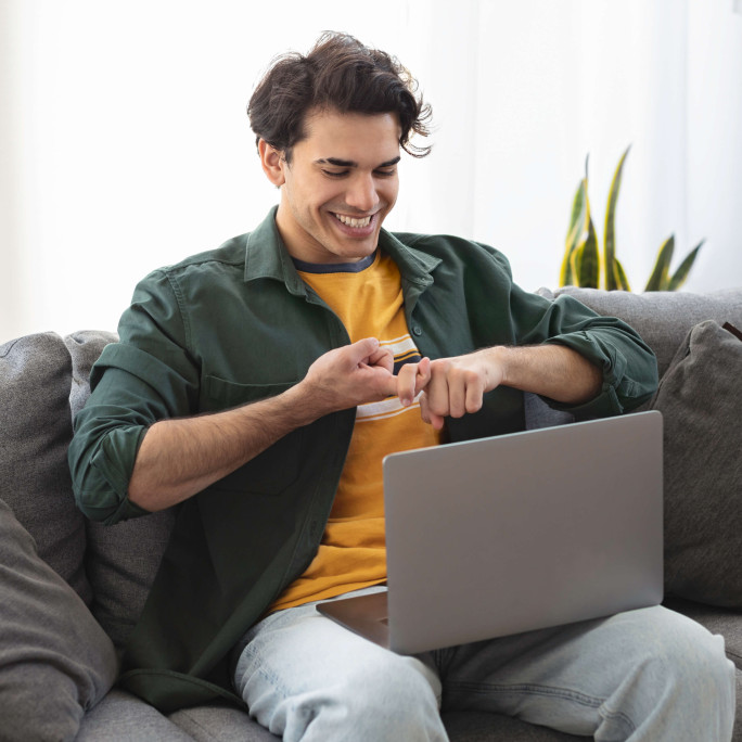 man on sofa smiling doing sign language on laptop