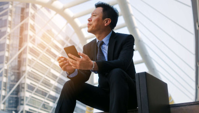 Asian man in a suit sitting on steps with a brief case and phone in hand looking up to the sky