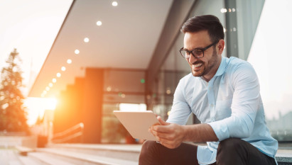 man smiling with glasses wearing smart clothes sitting outside on steps with tablet in hand