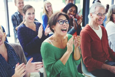 group of people sitting down in causal clothing applauding while laughing and smiling