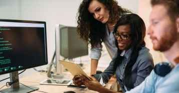 two women working together with man working on computer
