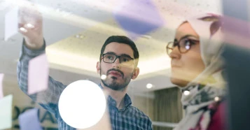 window view of two people discussing the messages observed on the post-it notes