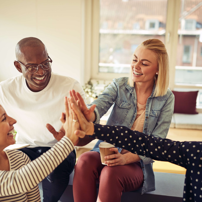 eye level view of four people high-fiving in a casual working environment