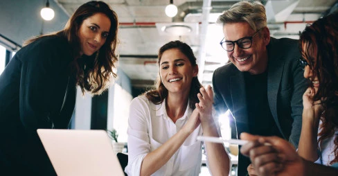 eye level view of four people smiling and wearing smart clothing surrounding laptop