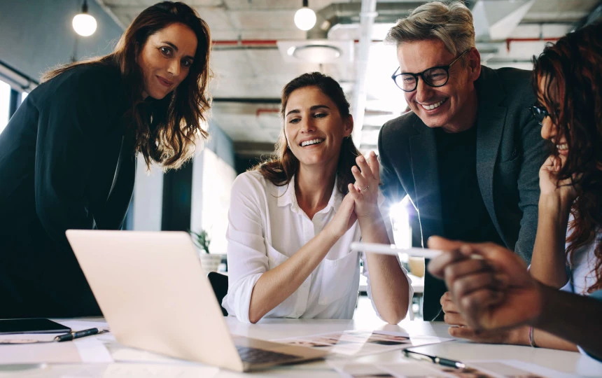 eye level view of four people smiling and wearing smart clothing surrounding laptop