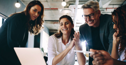eye level view of four people smiling and wearing smart clothing surrounding laptop