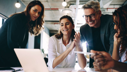 eye level view of four people smiling and wearing smart clothing surrounding laptop