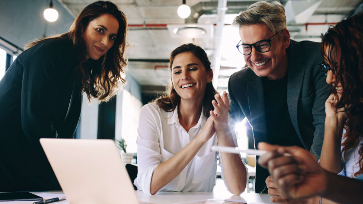 eye level view of four people smiling and wearing smart clothing surrounding laptop