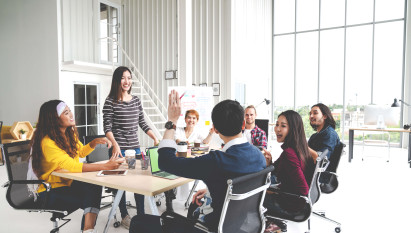 seven people smiling at meeting table with a man's arm raised