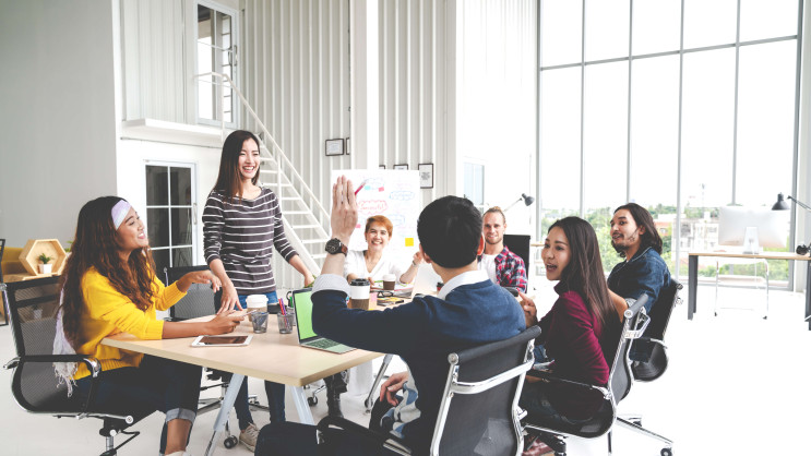 seven people smiling at meeting table with a man's arm raised