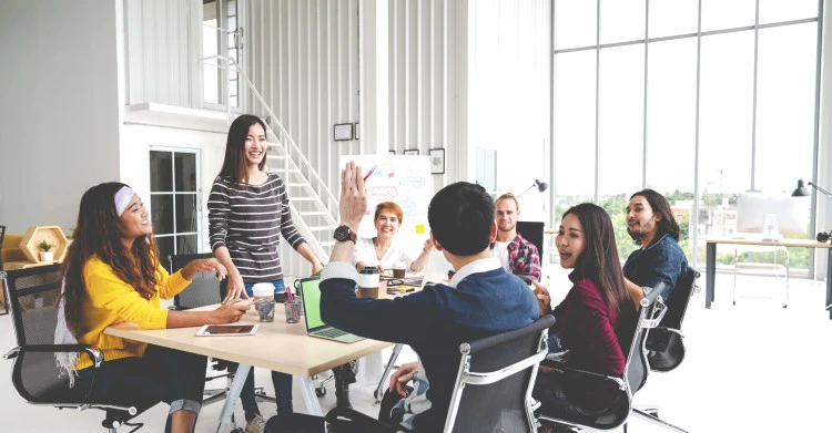 seven people smiling at meeting table with a man's arm raised