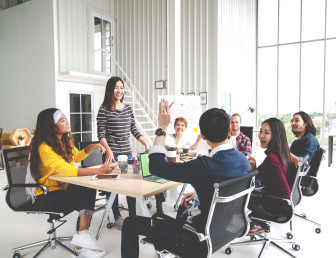 seven people smiling at meeting table with a man's arm raised