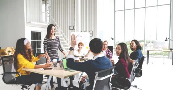 seven people smiling at meeting table with a man's arm raised
