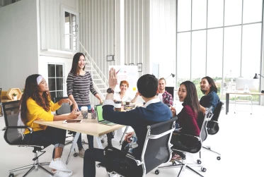 seven people smiling at meeting table with a man's arm raised