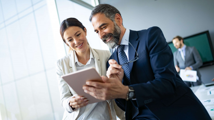 two people smiling while looking at tablet device