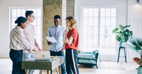 four people in gathered round a small table with a laptop in a casual office setting