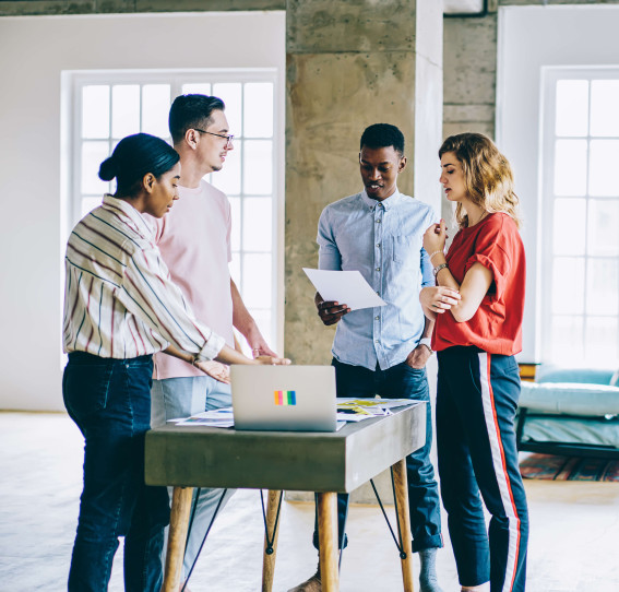 four people in gathered round a small table with a laptop in a casual office setting