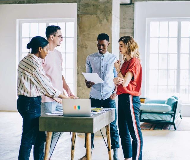 four people in gathered round a small table with a laptop in a casual office setting