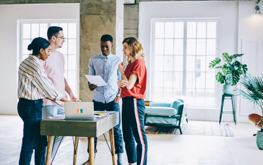 four people in gathered round a small table with a laptop in a casual office setting