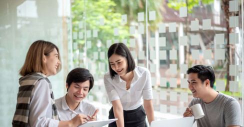 four people smiling sitting round a desk with a laptop