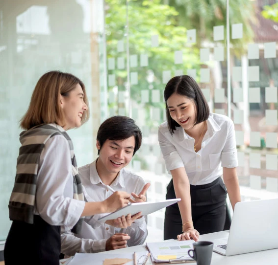 four people smiling sitting round a desk with a laptop
