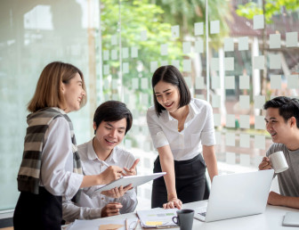 four people smiling sitting round a desk with a laptop