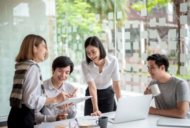 four people smiling sitting round a desk with a laptop