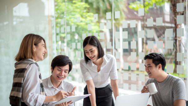 four people smiling sitting round a desk with a laptop