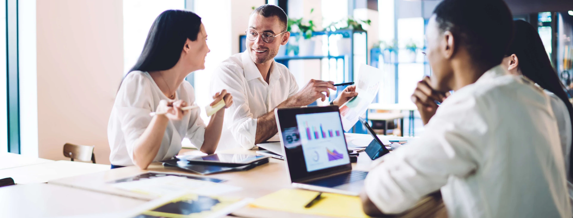 four people in smart clothing sitting in a office communal area with laptops and documents