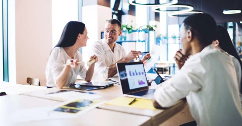 four people in smart clothing sitting in a office communal area with laptops and documents