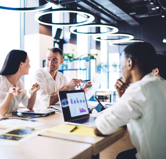 four people in smart clothing sitting in a office communal area with laptops and documents