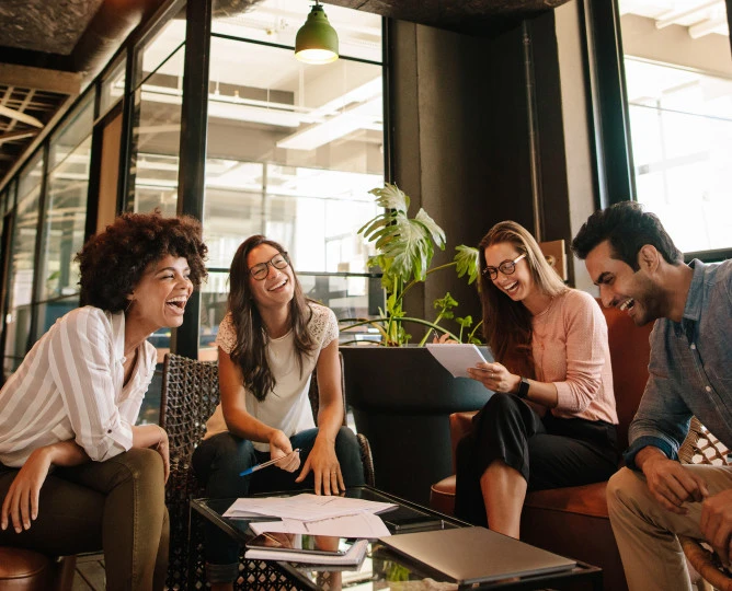 A froup of four colleague in an office setting. They are gather around a table covered with work-related documents. 
