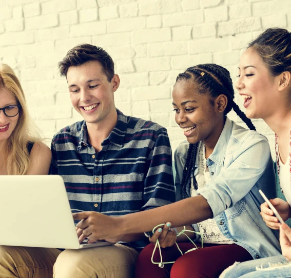 four young people smiling wearing casual clothing looking at a laptop