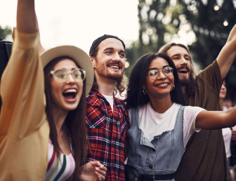 four people outdoors in a festival setting smiling and cheering with their hands up