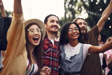 four people outdoors in a festival setting smiling and cheering with their hands up