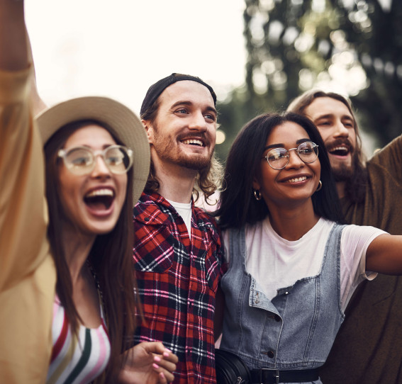 four people outdoors in a festival setting smiling and cheering with their hands up