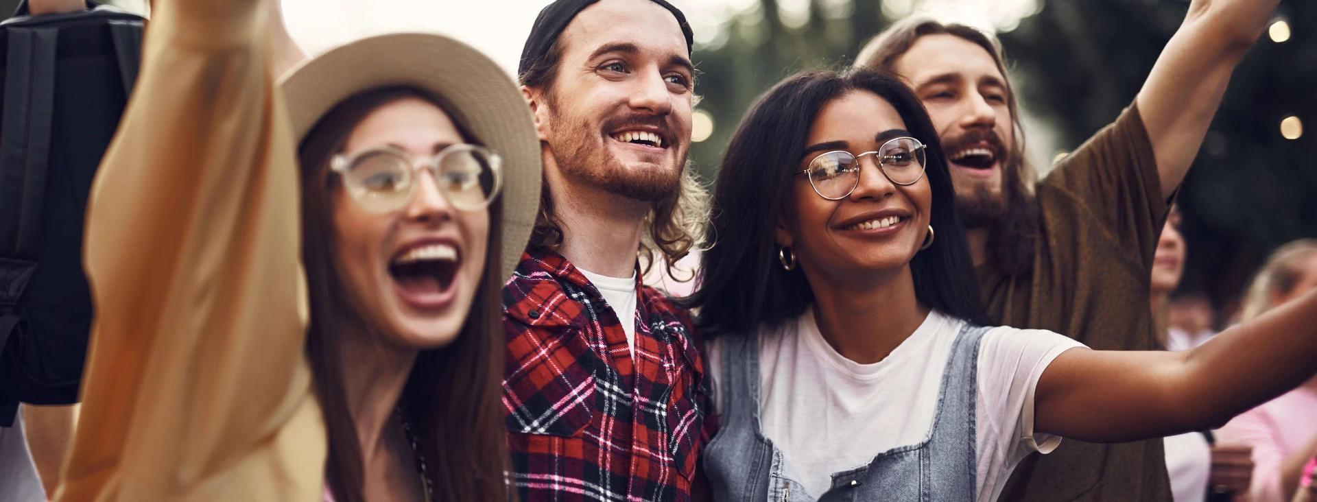 four people outdoors in a festival setting smiling and cheering with their hands up
