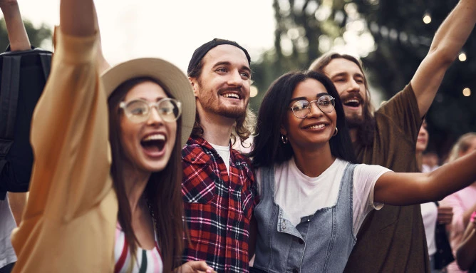 four people outdoors in a festival setting smiling and cheering with their hands up
