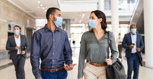 two people walking and talking with masks on with two people in background with masks on