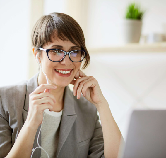 eye level view of woman sitting in front of laptop with headphones in smiling
