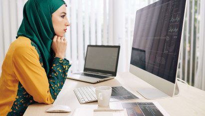 woman in hijab analysing data on apple mac with laptop and notes on the desk