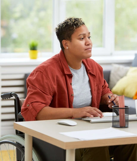 woman in a wheelchair wearing casual clothes working at a desk at home