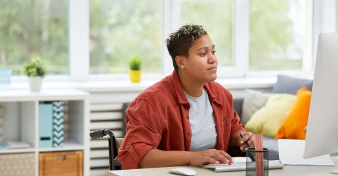 woman in a wheelchair wearing casual clothes working at a desk at home