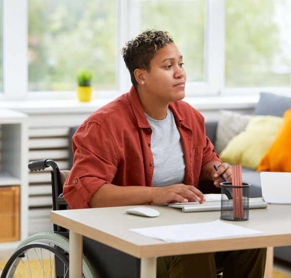 woman in a wheelchair wearing casual clothes working at a desk at home