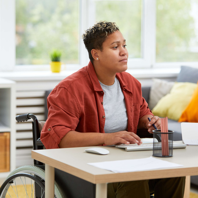 woman in a wheelchair wearing casual clothes working at a desk at home