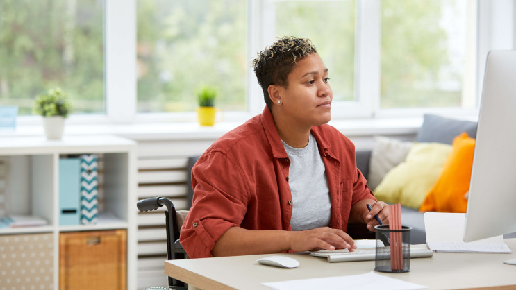 woman in a wheelchair wearing casual clothes working at a desk at home