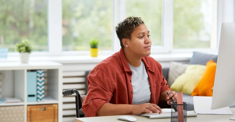 woman in a wheelchair wearing casual clothes working at a desk at home
