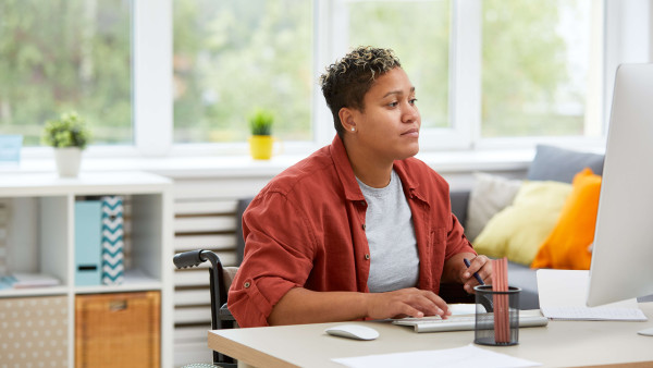 woman in a wheelchair wearing casual clothes working at a desk at home