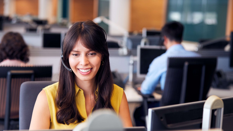woman in office smiling and sitting at desk with headset on